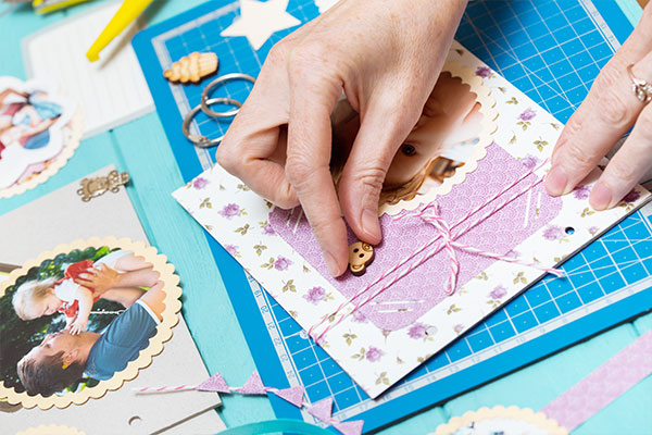 Mani che compongono una pagina di scrapbooking con foto e decorazioni